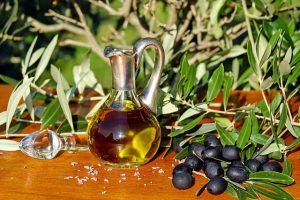 Aceita de oliva en una aceitera rodeada por aceitunas y hojas de olivo